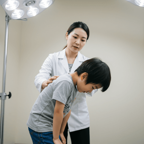 우리 아이, 내 척추는 괜찮을까? 어린이 & 어른 척추측만증 완벽 예방 & 치료 가이드! 3 아담스 전방 굴곡 검사를 하는 아이와 이를 관찰하는 부모 또는 의료인의 모습을 담은 사진